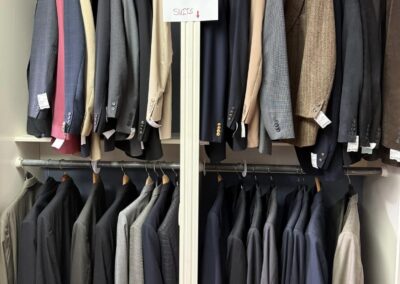 A closet neatly displays various colored sportcoats and suits, organized on hangers with a sign indicating the sections for easy browsing.