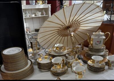 A collection of elegant porcelain dishes with gold accents, floral patterns, and a decorative paper parasol displayed on a table.