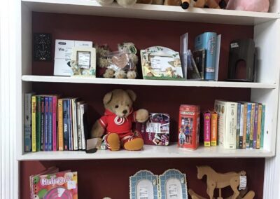 A shelf filled with teddy bears, books, and toys, including a rocking horse, colorful notebooks, photo frames, and Snoopy figures.