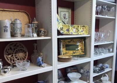 Shelves filled with various decorative items, including ceramics, glassware, and small art pieces. A colorful floral tray and a cat sketch are visible.