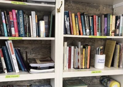 Bookshelves filled with various books and magazines, labeled fiction and non-fiction. A note on prices and a cup labeled "FREE Bookmarks" visible.
