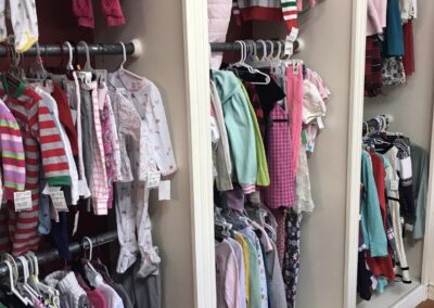 A children's clothing store display with various colorful outfits hanging on racks, showcasing a wide selection of baby and toddler attire.