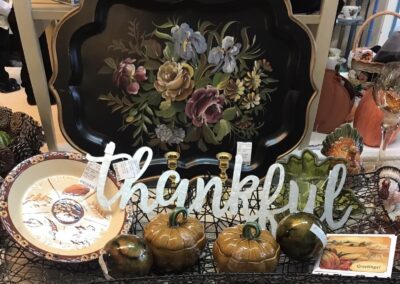 Artistic floral tray and Thanksgiving-themed decor, featuring "thankful" sign, ceramic pumpkins, and festive plates on display in a store setting.