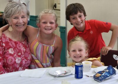 A person and three children smile at a table with snacks and drinks, appearing to enjoy a casual indoor gathering.