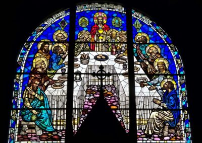 Stained glass window depicting the Last Supper with vibrant colors, featuring religious figures around a table, inside a church setting.