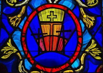 Stained glass window with vibrant blue, red, and yellow colors, featuring a cross design and floral patterns, symbolizing religious themes.