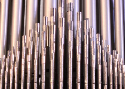 A close-up of silver organ pipes arranged in ascending order, reflecting light, creating an intricate and harmonious visual pattern.