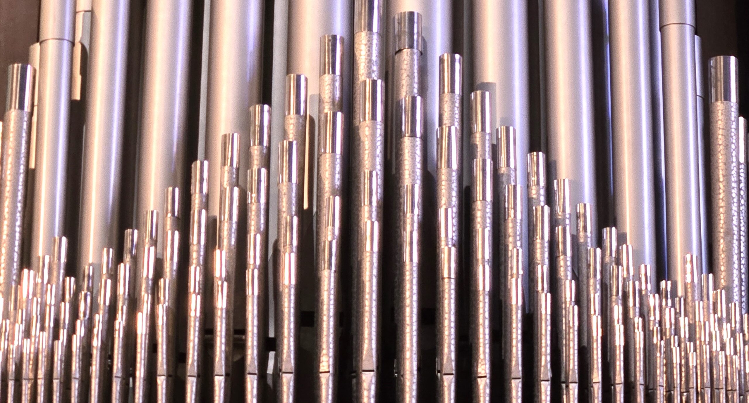 A close-up of silver organ pipes arranged in ascending order, reflecting light, creating an intricate and harmonious visual pattern.