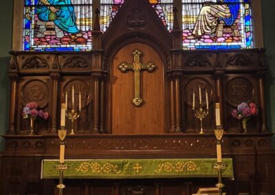 Stained glass depicting religious scene in a church. Ornate altar with candles and crucifix. Vibrant colors and intricate details enhance spiritual atmosphere.