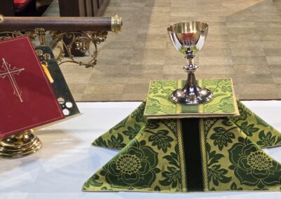 A chalice and religious book displayed on an altar, featuring intricate gold and green fabric with cross motifs in a sacred setting.