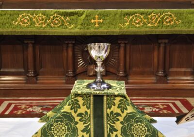 An ornate altar with a chalice covered by intricately embroidered green and gold fabric inside a church setting.